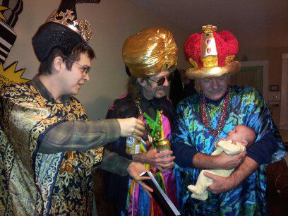 three grown men dressed like the three wise men from the bible, handing beer to a baby