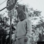 grayscale photography of man with paper bag on his head